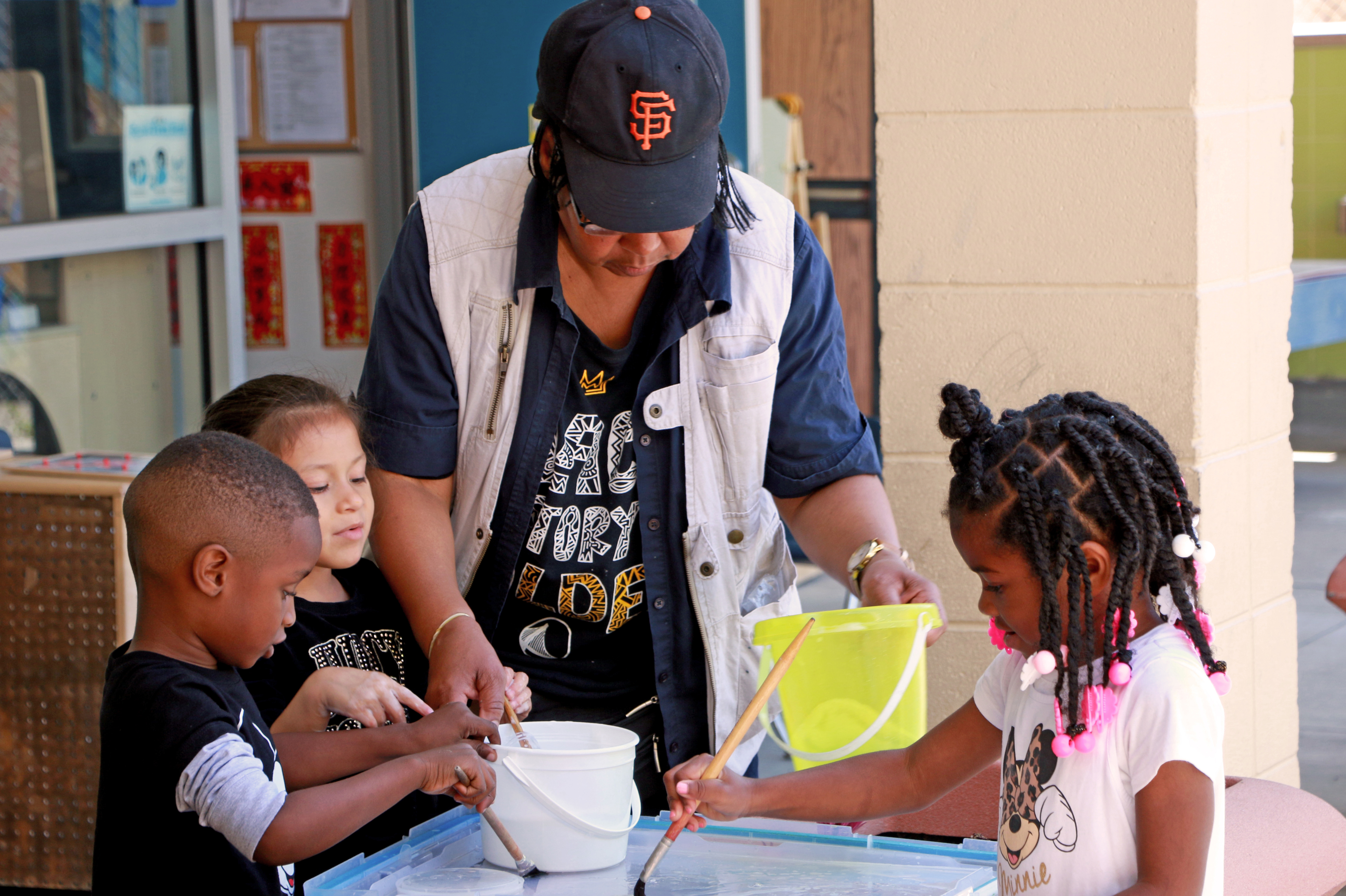 Woman helping three children paint