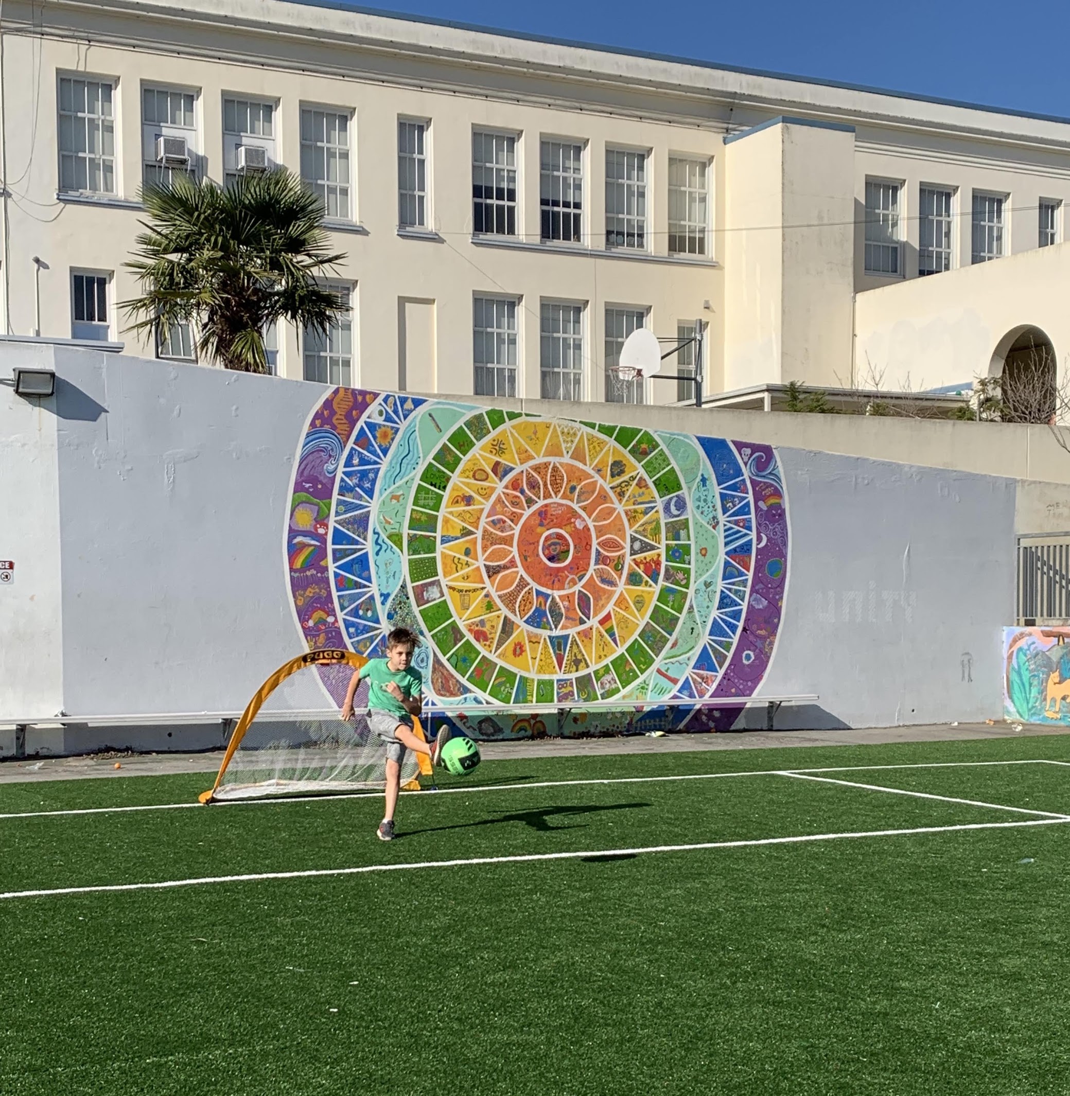 Boy kicking a soccer ball in front of Alvarado Mural