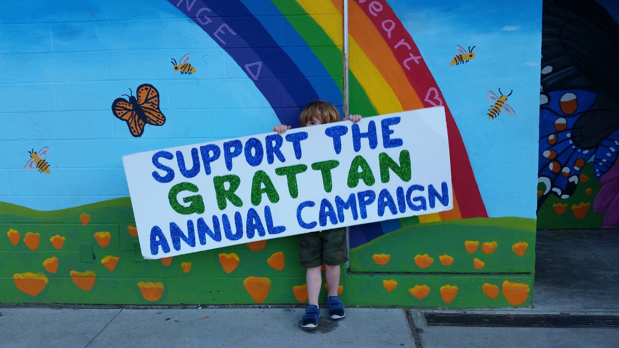 Young boy holding annual campaign sign with colorful mural in background