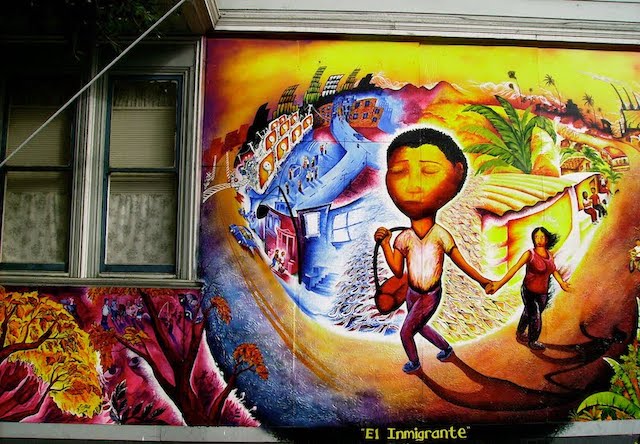 Photo of a San Francisco street mural painted on a building by Joel Bergner called "El Inmigrante," depicting a man walking on a road towards an urban setting and away from a countryside setting as he is letting go of a woman's hand.