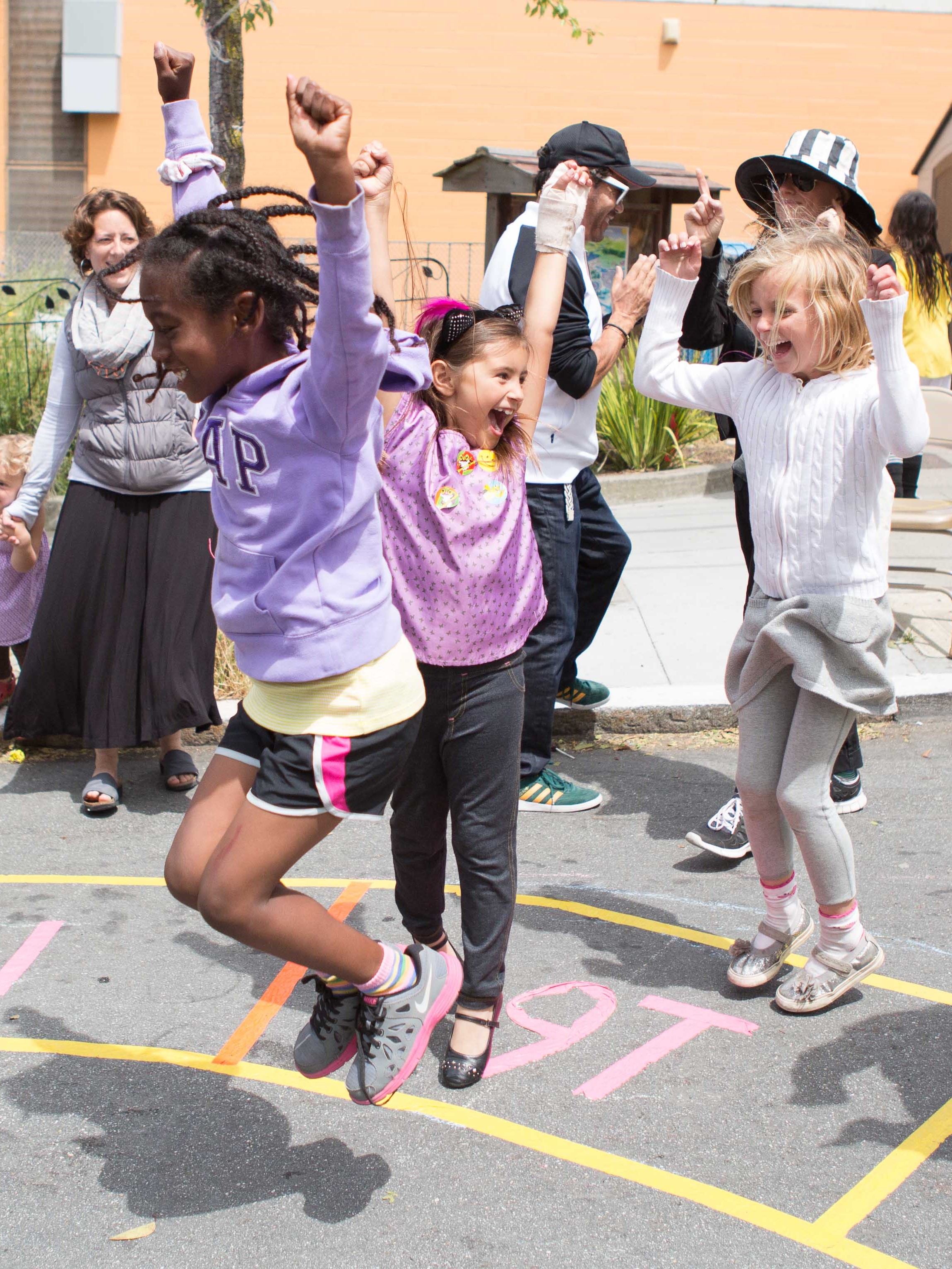 Three girls jumping joyfully after winning a game at an outdoor school festival