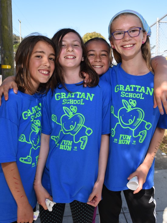 Four girls in matching t-shirts standing arm in arm at an outdoor school fitness event