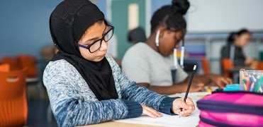 Student at desk writing on paper with pencil