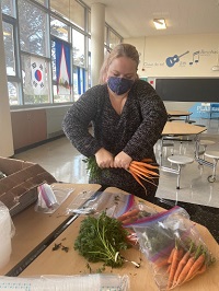 A volunteer preps carrots for a take-home meal kit at Marshall High School