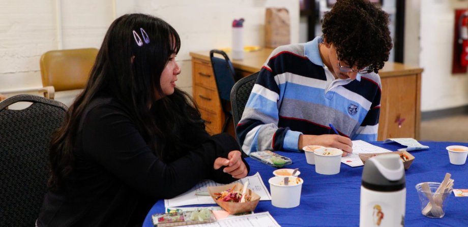 Two high school students tasting school food samples and filling out a feedback form.