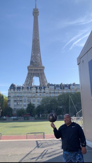 A man is spinning a basketball with one finger, standing in front of Eiffel Tower