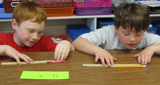 Two 3rd grade students measuring crayons and pencils with rulers