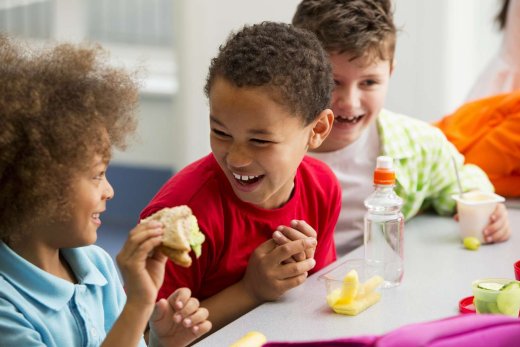 Three seven-year-olds laughing and eating lunch together