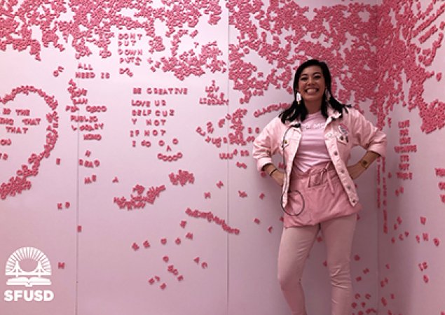 Sydnie in front of pink wall covered with letters