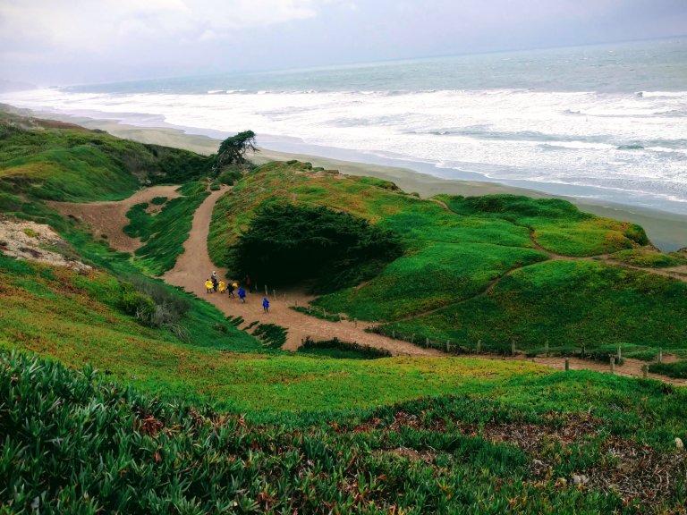 People hiking on a downhill trail next to the ocean.