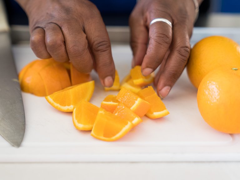 A hand is moving orange slices on a cutting board.