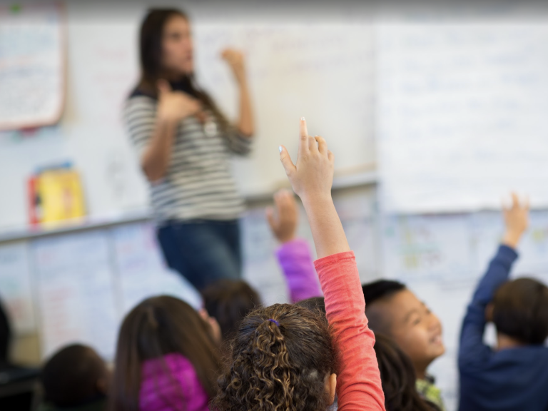 Teacher in classroom with students raising their hands