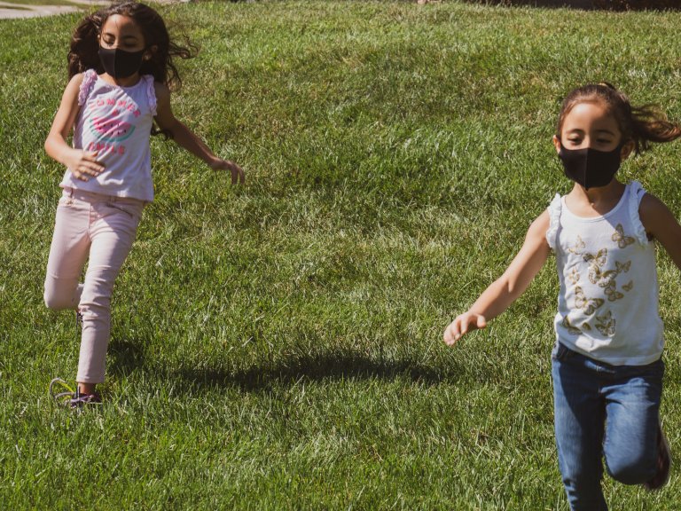 Two children in masks running across grass