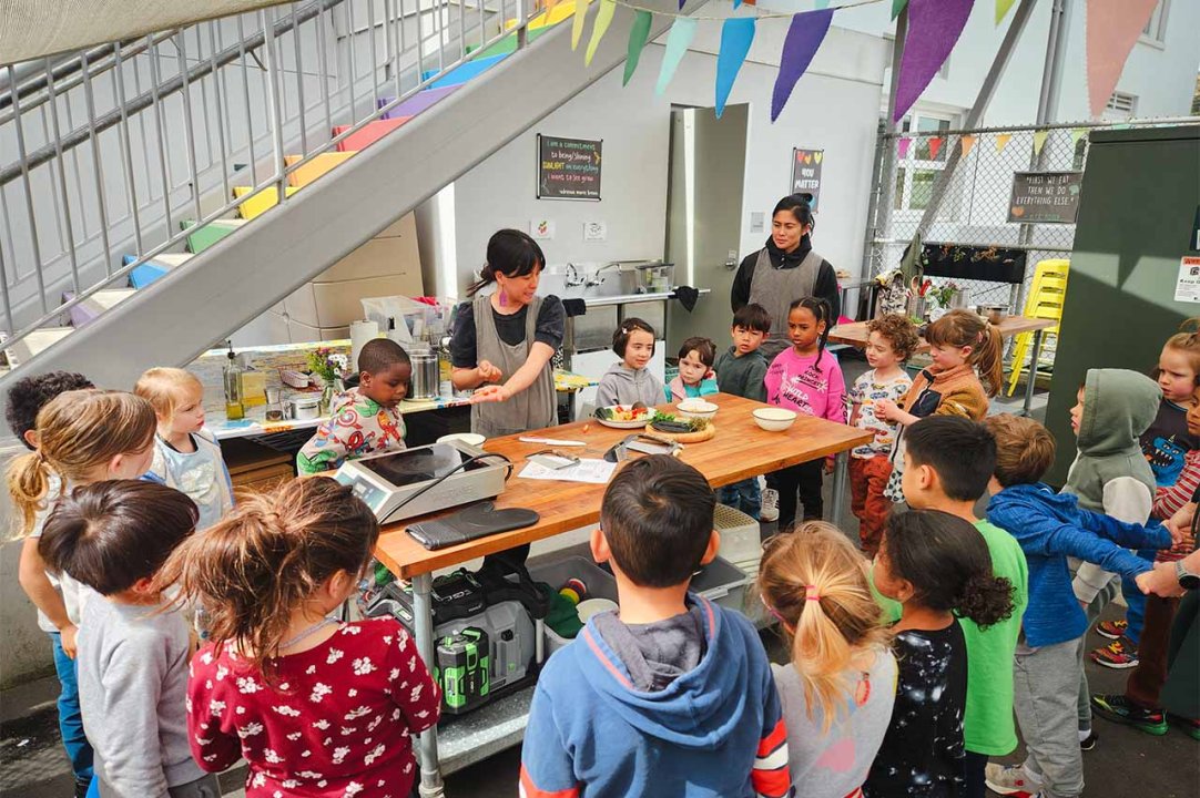 Ms. Joyce teaches a class of kindergarteners cooking in an outdoor space on-site.