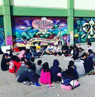 Middle school students sitting in a circle in front of a mural