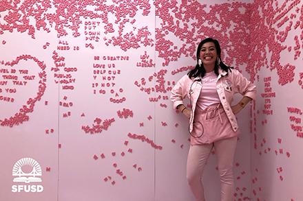 Sydnie in front of pink wall covered with letters