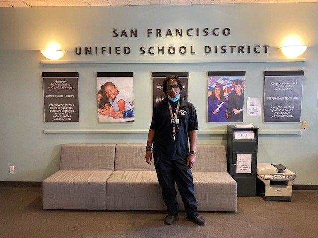 Tobias Cain, a security aide from Marshall Elementary School, poses in front of a wall at the SFUSD central office
