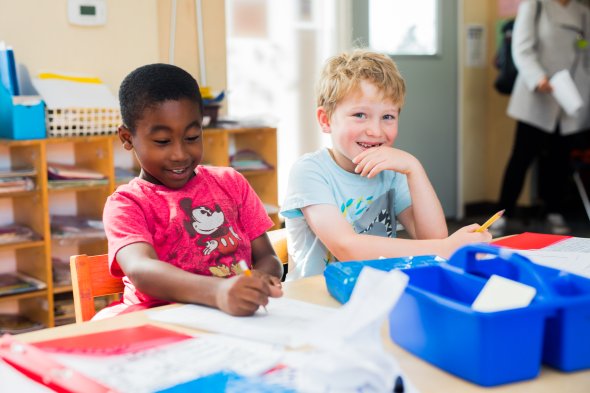 Two male students sit at a table and smile.
