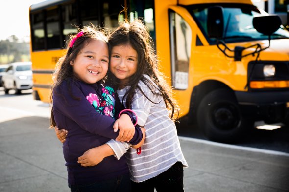 Students hugging in front of a school bus