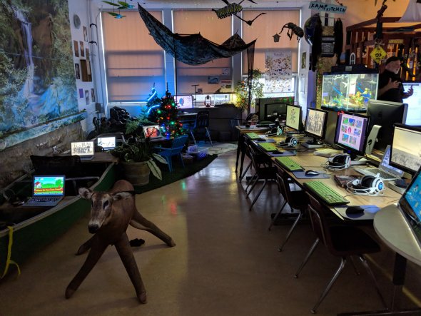 Computer lab with computers at tables and decorations, including a canoe and a life-size deer