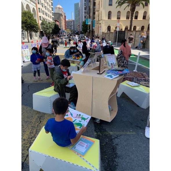 Students and families reading books at an open-air reading room by SFUSD Libraries on Golden Gate Avenue in the Tenderloin