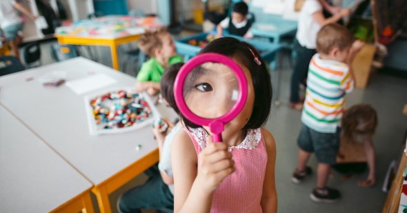Kindergarten student peering through magnifying glass
