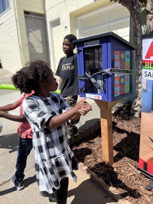 A child views a newly-completed Little Free Library at the Robinson residence between Castillo and Santos in the Visitacion Valley neighborhood.