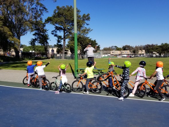 Eight students on bikes receiving instructions from an instructor standing in front of them