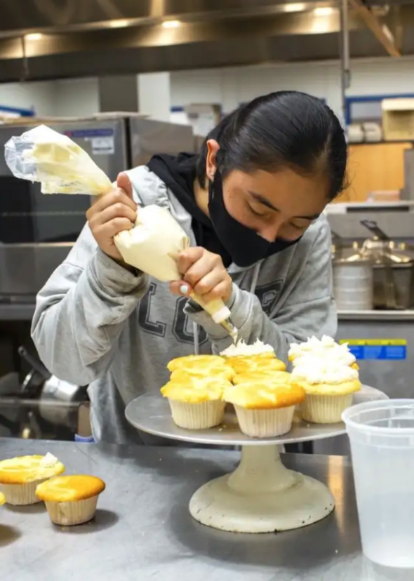 Culinary student puts icing on cupcakes in the John O'Connell High School kitchen.