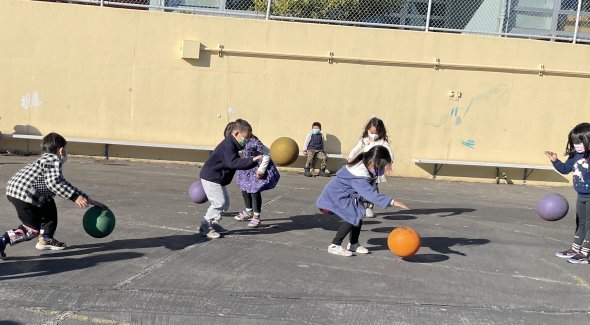 A small group of young students bouncing balls outdoors