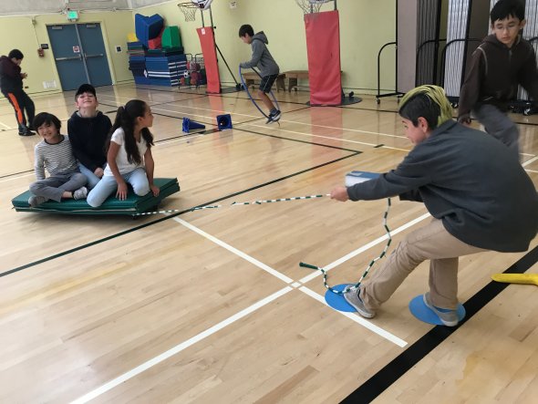 Three students being pulled on a makeshift sled by a fourth student  during PE class