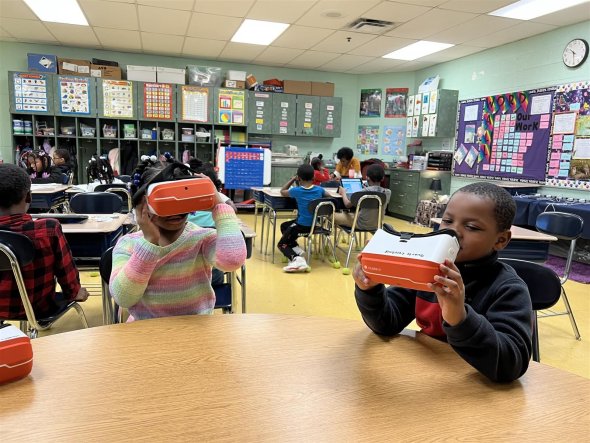 1st-grade classroom. Two students seated at a table using individual virtual reality head-sets