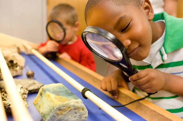  children looking at rocks with magnifying glass