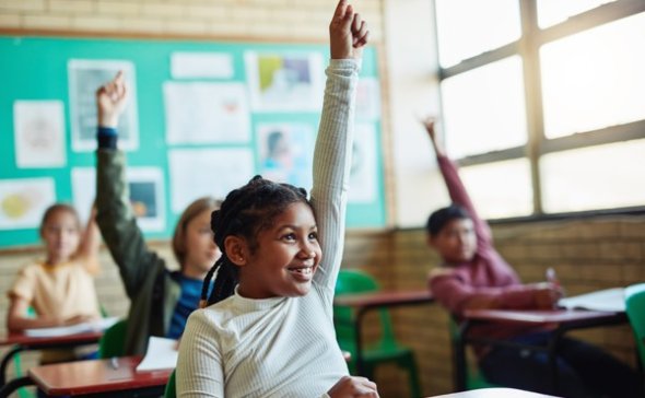 4th-grade student smiling and raising hand in class