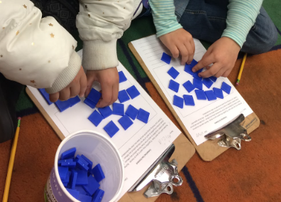 The hands of two young students arranging blue tiles.