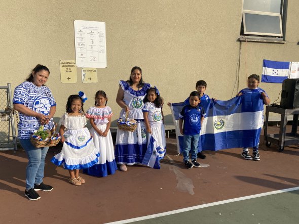 Guadalupe Elementary staff, parents, and students wearing traditional costumes from El Salvador and holding up the El Salvador flag.