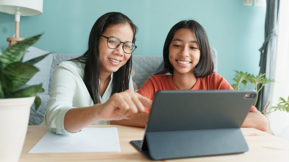 a parent and a student sitting side by side, smiling, in front of a computer