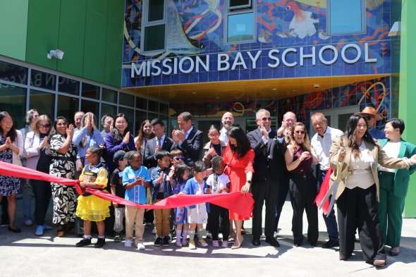 Group of leaders and students cutting red ribbon by school entrance