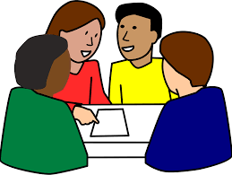 Four people collaborating at a table. One person points to a paper on the table.