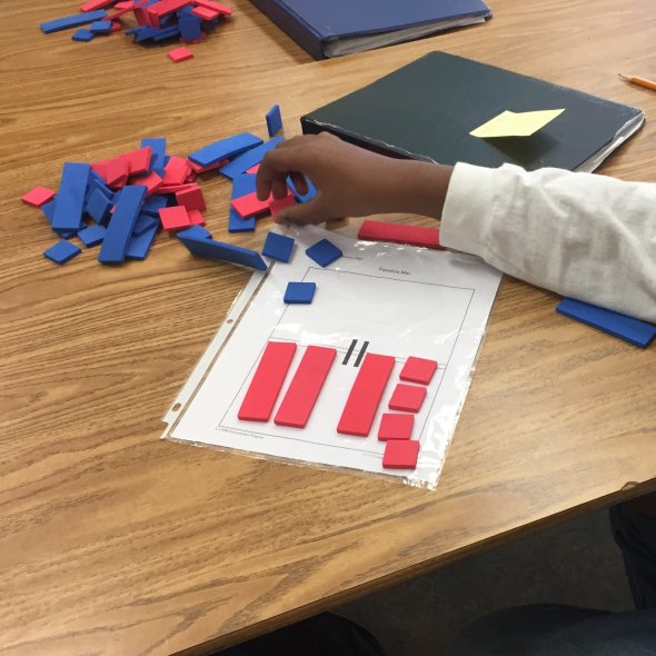 Student working with algebra tiles on equation mat