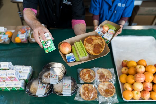 Close-up of staff serving oranges, pizza, celery and milk for school lunch