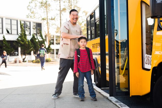 Parent/guardian with elementary school student in front of yellow school bus