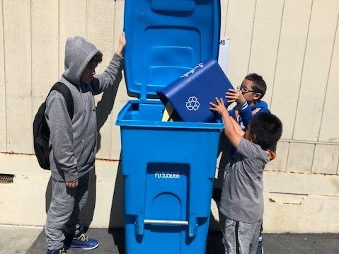 Three students throwing recycling into blue bin