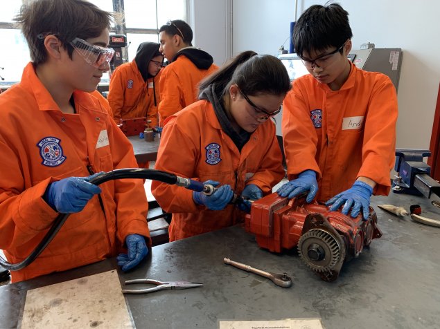 Three students work on a car engine together. 