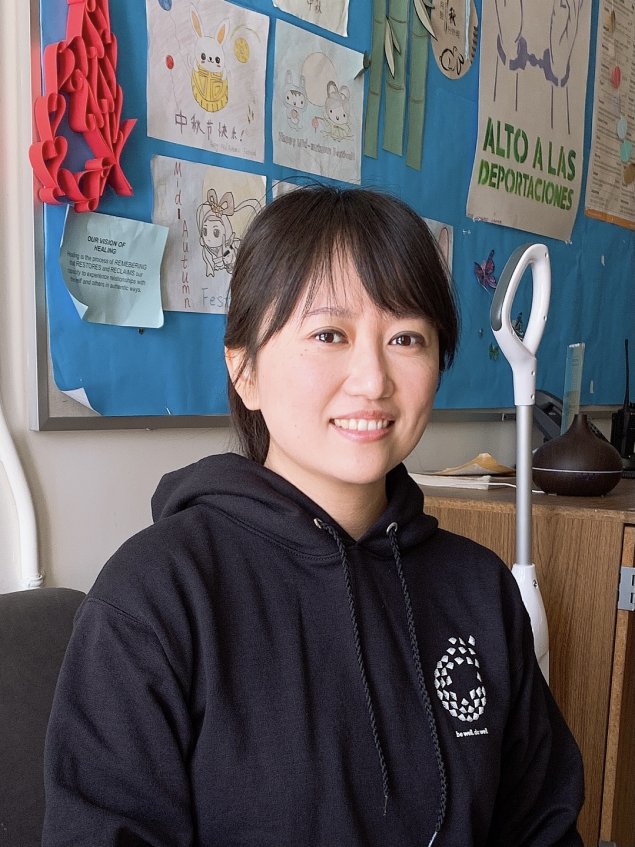 Asian woman with shoulder length dark brown hair and in a black sweatshirt with a Wellness logo.