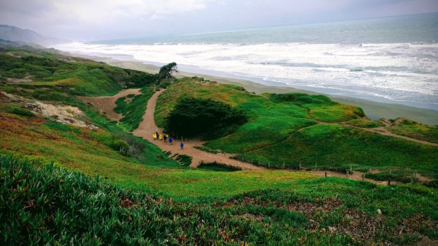 People hiking on a downhill trail next to the ocean.