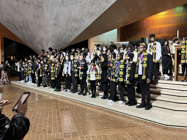 Students standing on steps of stage with their kente cloth stoles and medallions 