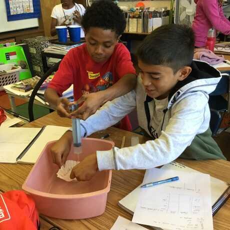 Two 4th-grade students engaged in a science experiment involving water and paper