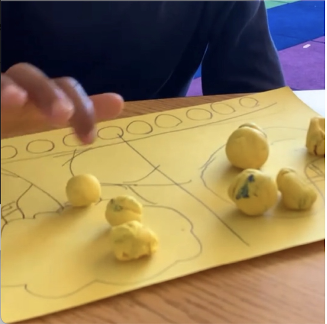 Student pointing at fruit on a yellow mat.