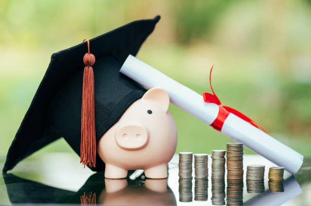 graduation cap with piggy bank, diploma and stack of coins